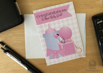Baby bottle, pink block, pink bow, pink diaper pin, diamond background, Text reads "Congratulations! A New Baby Girl"